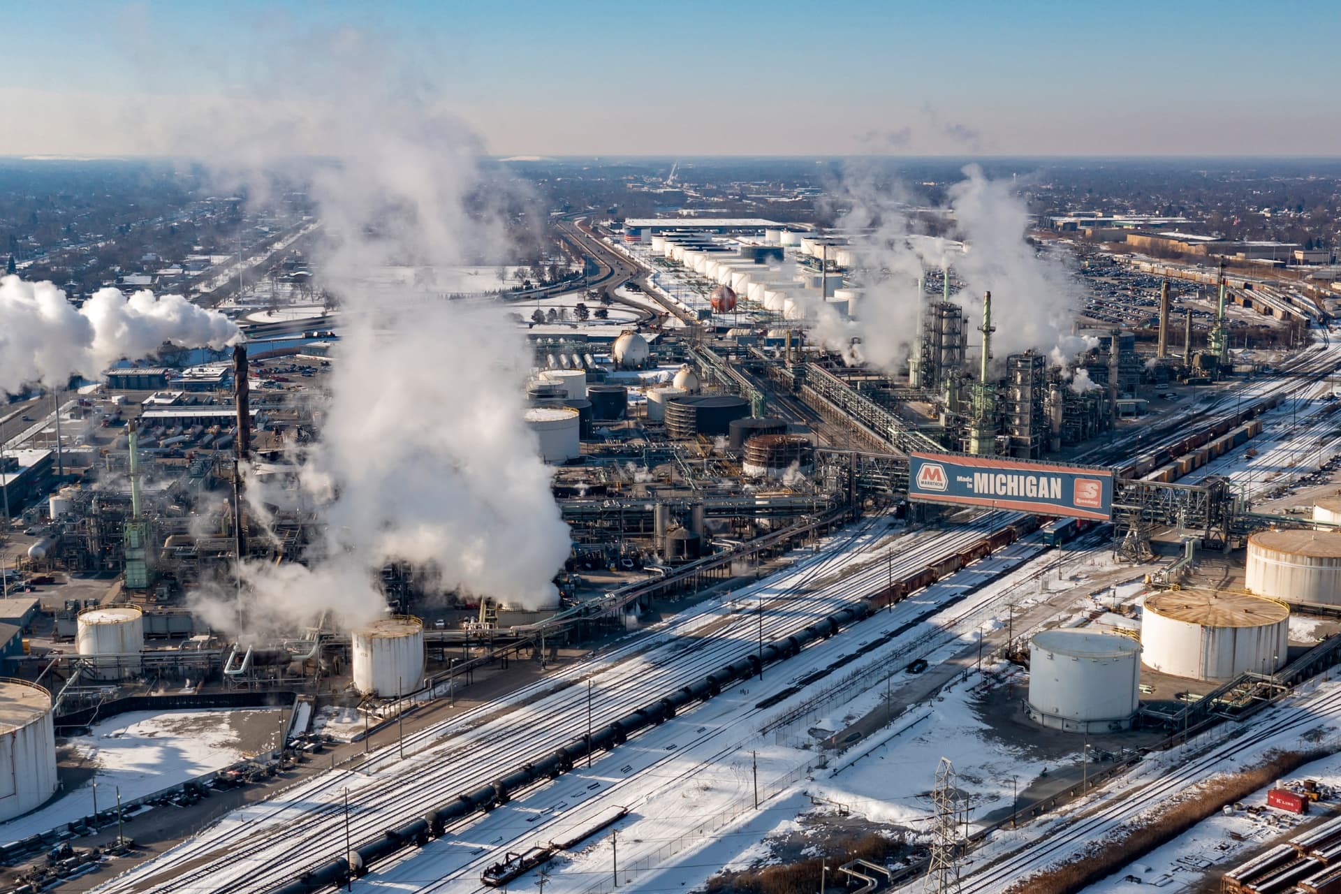 Industrial Midwest refinery with steam rising above snow-covered rail yards